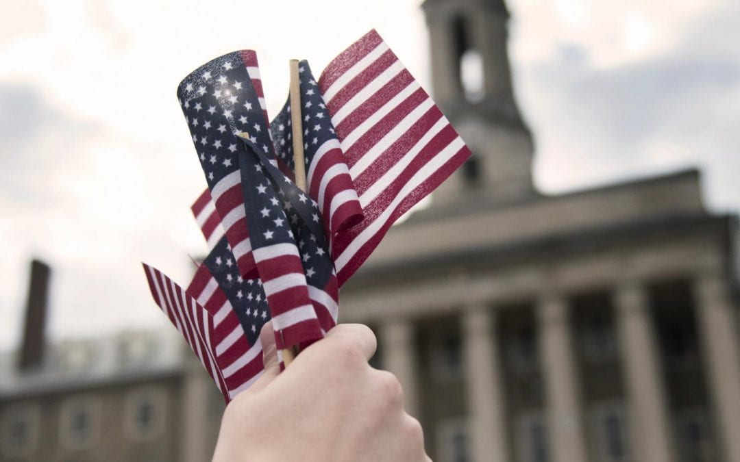 Hand holds a handful of small American Flags, with large building in the background